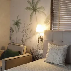 My 'Whispering Willow' wallpaper bringing the untamed outdoors into a cozy bedroom corner. The design features soft, hand-painted style palm trees that create a calming and natural atmosphere.