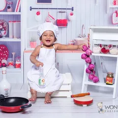 A little chef in the making. This kitchen setup is always a hit, with a chef's hat, apron, and plenty of props for the baby to interact with, leading to wonderfully expressive photos.