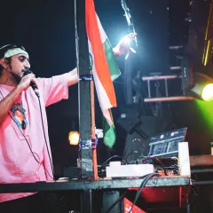 Addressing the crowd on the mic during a Republic Day party, with the tricolor flag proudly displayed.