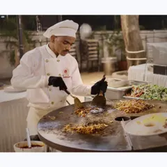 Tossing the wok! A chef skillfully prepares a stir-fry on a large flat-top grill, a classic live station that always draws a crowd with its delicious aromas and fast-paced action.