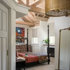 This tranquil bedroom in Saratoga features a stunning four-poster bed set against a backdrop of warm, neutral tones. The vaulted wooden ceiling and large window add to the room's airy and spacious feel, creating a perfect retreat.