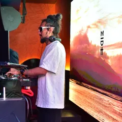 A side profile showing me focused on the mix, with abstract, colorful visuals creating a scenic backdrop on the LED screen.