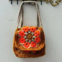 This small, rustic-looking sling bag features a floral granny square pattern on the flap, made with earthy orange and beige tones.