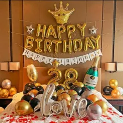 A surprise 28th birthday bedroom decoration. The setup features "Happy Birthday" and "love" foil balloons, a crown, and champagne bottle foils over a bed covered in balloons and rose petals.