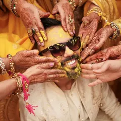 A close up of the groom's Haldi moment. Surrounded by the hands of his loved ones, his joyful smile shines through, even with sunglasses on.