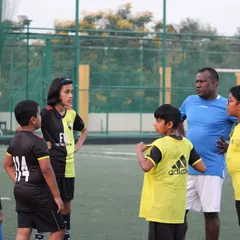 A coach leads a post-drill discussion with a group of young players, including boys and girls. We believe in breaking down the game and ensuring every child understands the strategy behind the skills.