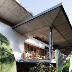 A view of an upper-level balcony at the House of Canopies, tucked beneath a sweeping concrete roof. This private outdoor space feels both protected and open, offering elevated views of the garden through the surrounding foliage.