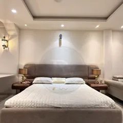 This bed showcases a minimalist aesthetic with its clean lines and simple, curved headboard. The rich brown fabric and matching wooden side tables create a cohesive and calming atmosphere.