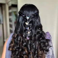 A whimsical and modern hairstyle perfect for a fun-loving bride. This look features a braided half-updo with bouncy curls, adorned with colorful butterfly clips.