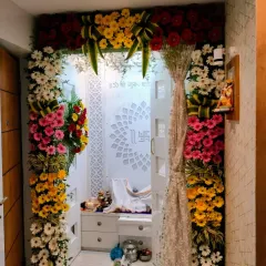 This decoration shows how we can enhance a modern prayer space. A colorful arch of fresh gerbera daisies frames the entrance to the mandir, adding a festive and respectful touch to the home's sacred corner.