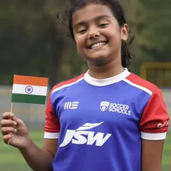 A smiling young girl holds the national flag. We believe in empowering girls through sport, building their confidence and skills.