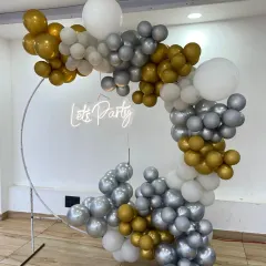 A beautiful ring backdrop with a 'Let's Party' neon sign. The arch is decorated with an asymmetrical garland of chrome silver, gold, and white balloons, perfect for a chic party.