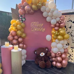 A warm and inviting terrace setup with a pink backdrop and a balloon arch in gold, white, and rose gold tones.
