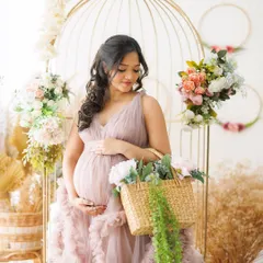 A romantic and whimsical scene, with the mother-to-be surrounded by flowers, a golden birdcage, and a basket of blooms. It's a perfect setup for a fairytale-inspired shoot.