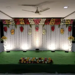 A simple yet beautiful stage design with a clean white drape backdrop. The colorful floral valance across the top adds a touch of brightness, making it a versatile choice for any wedding event.