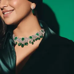Our take on bringing home the Christmas cheer. A smiling model wears a magnificent emerald and diamond choker, glowing against a green background.