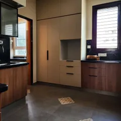 A modern kitchen featuring a mix of materials, including wood-finish and beige laminate cabinets, a black granite countertop, and patterned floor tiles. The design balances functionality with aesthetic details.