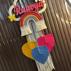 A colorful and cheerful nameplate for 'Raavya'. This design combines a classic rainbow with multi-colored macrame hearts and delicate butterfly accents, all made with natural cotton yarn.