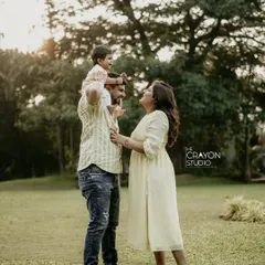A complete family portrait doesn't have to be posed. Here, a mother looks on with love as her husband gives their child a ride on his shoulders, creating a beautiful, candid moment of connection during their outdoor session.