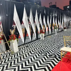 A stylish way to partition an outdoor event space. This setup uses a black and white chevron floor runner alongside a wall of black and white drapes, with red floral arrangements adding a pop of color.