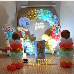 A personalized Cocomelon first birthday party for Aadvik. The decoration includes a circular balloon arch, multiple character cutouts, light-up marquee letters for the name, and a custom sign.