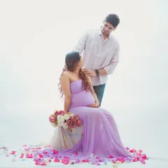A romantic couple maternity shoot with a light and airy feel. The soft lavender gown and minimalist white background create a serene atmosphere, focusing on the connection between the expecting parents.