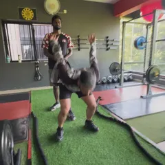 A client performs battle rope slams under the watchful eye of a trainer, a high-intensity exercise that works the entire body.