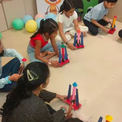 A group of kids sitting on the floor, each assembling their own colorful rocket. We provide all the pre-cut parts and decorations for personalization.