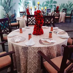 We believe guest comfort and experience are key. This elegant dining arrangement features a striking red rose centerpiece, classic tableware, and a tropical-themed backdrop, creating a sophisticated ambiance for an intimate gathering.