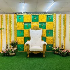 A simple and elegant puberty ceremony decor. The backdrop is a classic checkerboard of yellow marigolds and green fabric, with a grand white throne and banana plants completing the traditional look.
