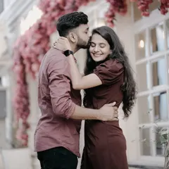 A tender moment with the groom kissing the bride's forehead, set against a backdrop of pink flowers and a cafe window.