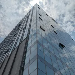 A worm's-eye view of a modern glass skyscraper, emphasizing its verticality against a cloudy sky. The operable windows are visible, a small but important detail that gives users control over their environment in a high-rise building.