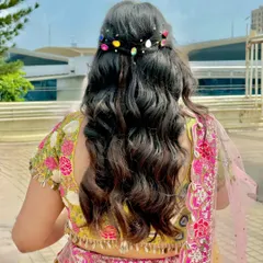 A playful and colorful hairstyle for a mehendi, with soft waves and multi-colored gem accessories.