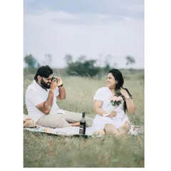 A picnic in a beautiful meadow. The groom-to-be playfully takes a photo of his partner, showing a sweet, candid interaction.