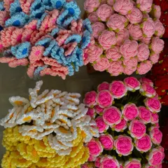 Piles of colorful crochet flower heads, including daisies and roses, waiting to be assembled into stems.