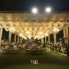 An expansive view of an elegant outdoor dining setup. I used a ceiling of white draped fabric and a grid of chandeliers to create a sense of a grand ballroom under the stars, with classic seating for a timeless feel.