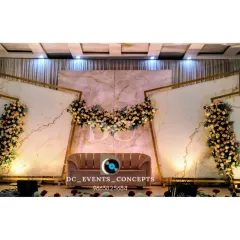 A modern and sophisticated wedding reception stage featuring white marble-patterned panels with gold geometric accents. The clean lines and delicate floral arrangements offer a chic and contemporary aesthetic.