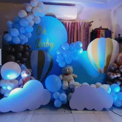An "Oh Baby" shower with a hot air balloon theme. The setup uses blue and brown balloons to create a sky-like scene, complete with cloud cutouts, teddy bears, and 'BABY' blocks.