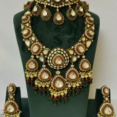 A heavy bridal necklace set available for rent, with a choker and a wide, cascading necklace. The design uses Kundan stones with red and green Meenakari details.