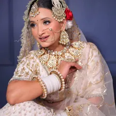 This angle highlights the beautiful bridal nath and jhumkas from the white lehenga set. The combination of white, gold, and a touch of red in the hair creates a modern yet traditional bridal aesthetic.