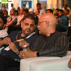 Two attendees engage in a quiet discussion during a conference session, sharing thoughts on the expert insights being presented.