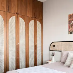 This bedroom features a beautiful custom wardrobe with arched cane panels and wood finishing. The design is a perfect blend of modern and traditional elements, creating a warm and personalized space.