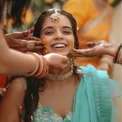 A beautiful candid shot of the bride's joyful expression as her friends and family apply turmeric paste during her Haldi ceremony.