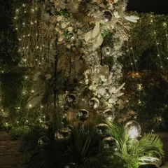 A stunning floral installation for an evening event, combining white flowers, dried palms, and silver baubles. The entire arrangement is interwoven with fairy lights, making it sparkle in the dark.