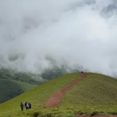 A group of trekkers on a distant ridge, dwarfed by the scale of the Netravathi landscape. It shows the true grandeur of the Western Ghats.