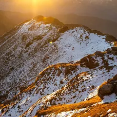 Another perspective of the sun-kissed mountains in Uttarakhand. This aerial shot showcases the layered ridges and the warm glow on the snow, capturing the immense and peaceful landscape from a unique angle.