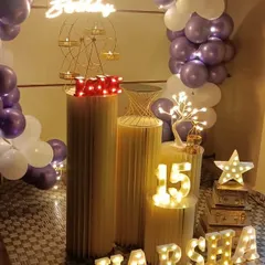 A detailed view of the props used for a 15th birthday. You can see the illuminated number '15', a light-up star, a miniature Ferris wheel candle holder, and a small lit tree, all arranged on different-sized pedestals.