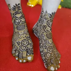 This design for the feet features a mix of floral patterns and checkerboard fills, with the toes fully covered in henna for a traditional finish.