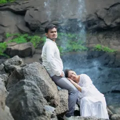 A creative and tender pose during a waterfall maternity session. The mother-to-be rests her head gently on her partner's leg, showcasing their comfortable intimacy and connection amidst the rugged, natural beauty of the location.