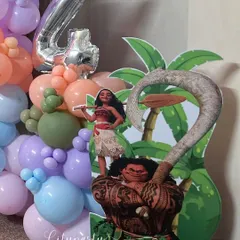 A 'Moana' themed birthday decoration for a 4th birthday. This setup includes character cutouts of Moana and Maui, a large '4' foil balloon, and a tropical-colored balloon garland.